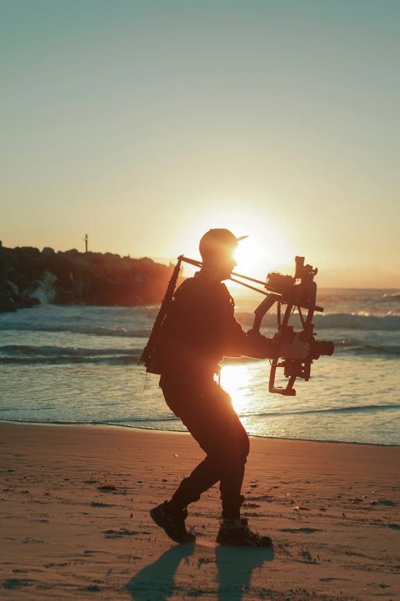 Silhouette of man holding a camera walking backwards on the beach