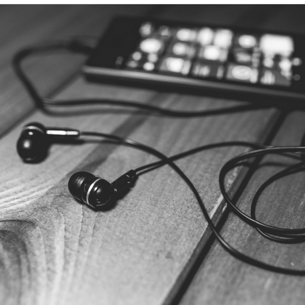 Black earbuds connected to s smartphone resting on a wooden table,